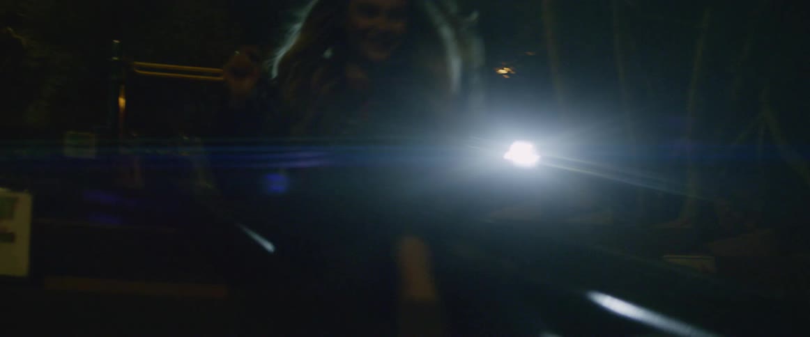 A couple holding flashlights as they ride down a slide in the dark