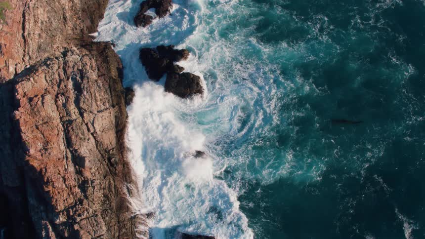 An aerial view of waves crashing on large rocks