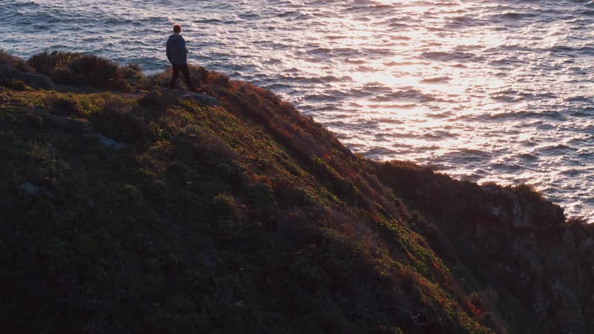 Man standing on a cliff next to the ocean at sunset