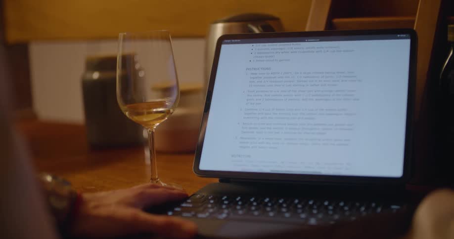A man drinks wine while using his tablet as a laptop