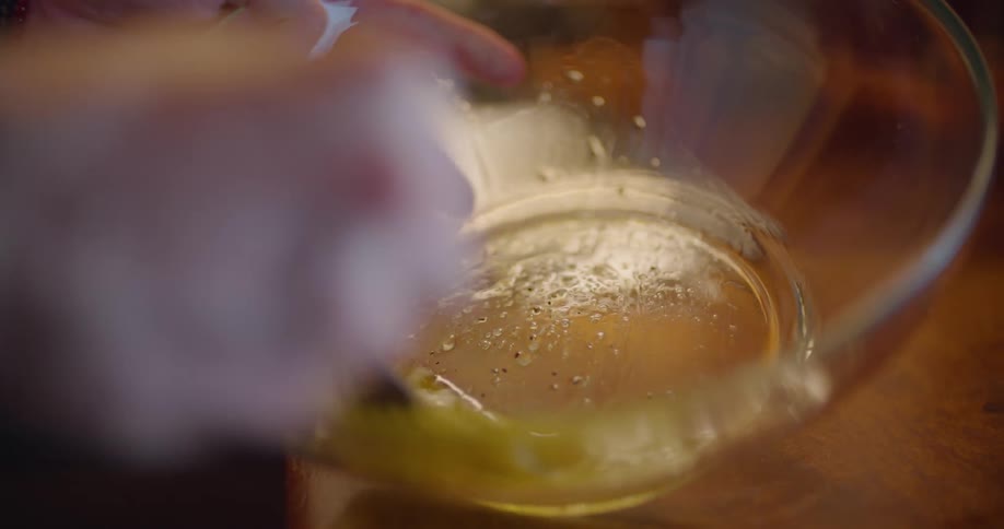 Hands hold a glass bowl and blend the yellow gold liquid inside