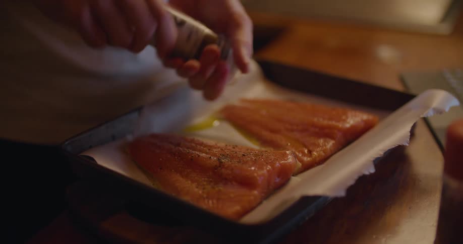 Person seasons fish fillets sitting on parchment paper on sheet pan