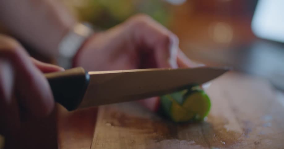 Piece of cucumber is being sliced and cut into chunks on a wooden cutting board
