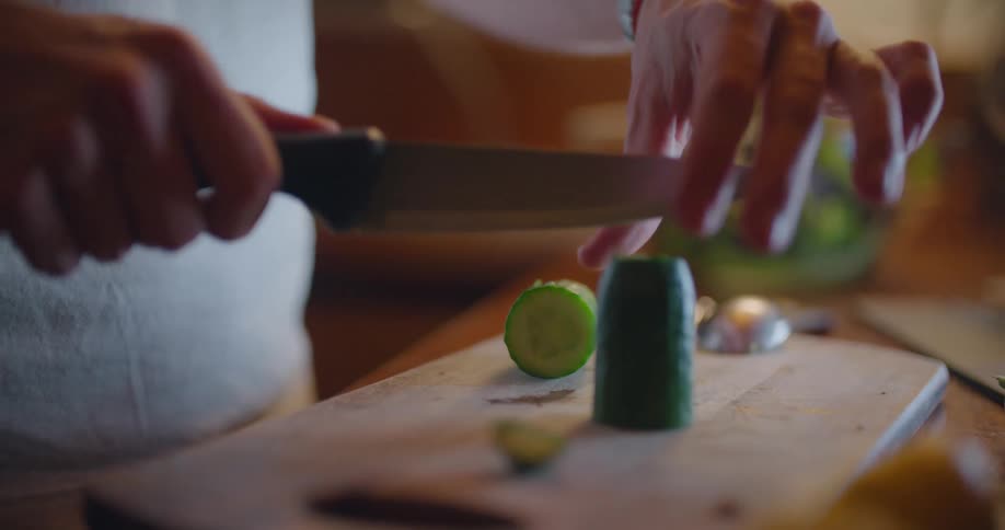 A person in a kitchen cutting a vegetable with a knife on a cutting board