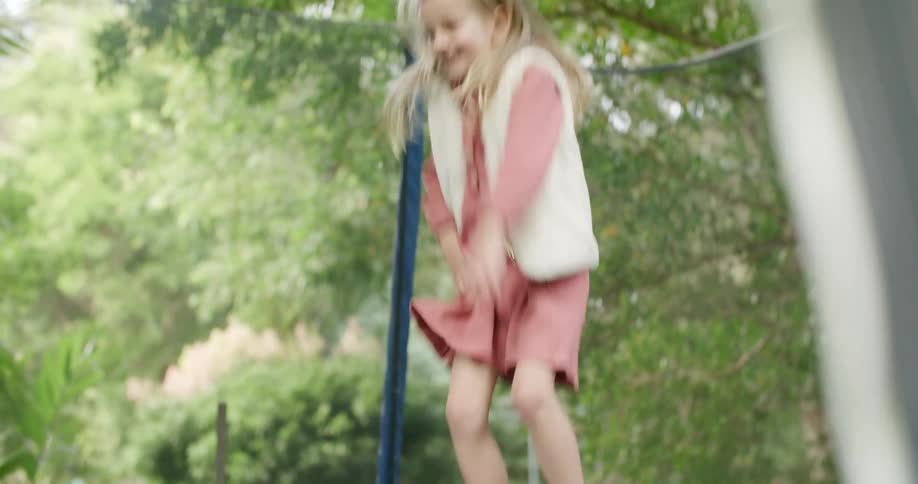 A girl jumping on a trampoline with trees the sky and clouds in the background