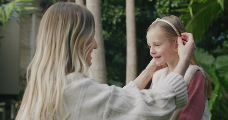 A woman putting a headband on a girls hair and kissing her with trees in the background