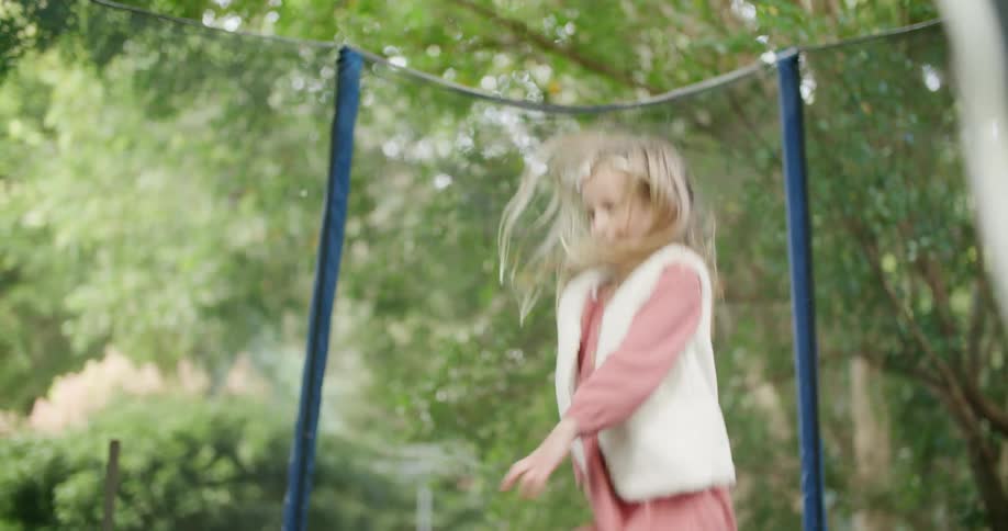 Girl with a pink dress jumping on a trampoline in the backyard