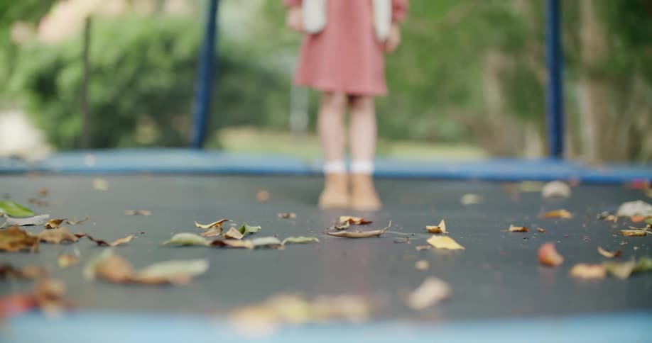 A young girl stands on a trampoline with leaves scattered across
