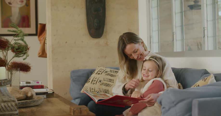 A woman and a girl in a room sitting on a couch reading a book
