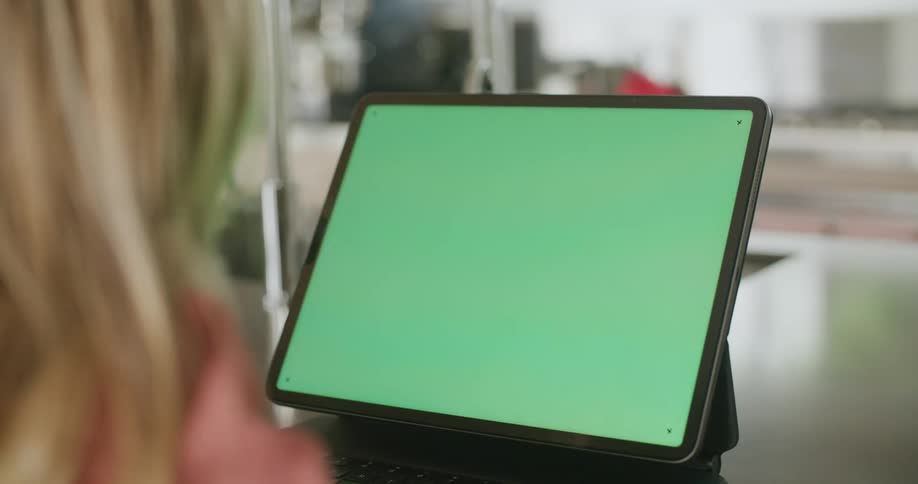 Blonde person sits in front of tablet set on stand on shiny kitchen counter across from sink