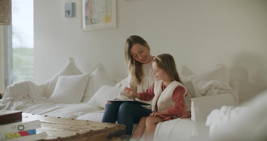 A woman and a girl in a room sitting on a couch looking at a tablet