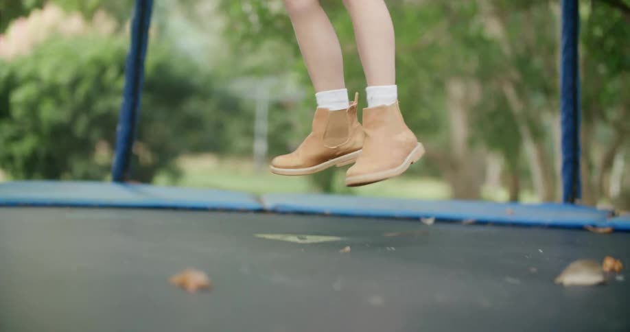 Girl in a pink dress jumping on a trampoline in the backyard