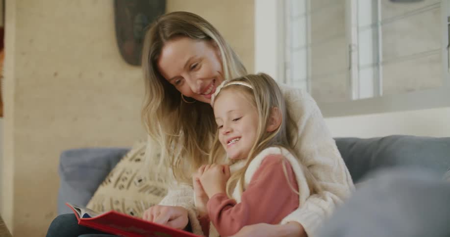 A woman and a girl in a room sitting on a couch reading a book