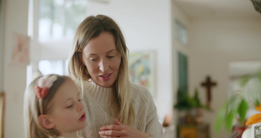 A woman laughs while helping her daughter do a task on a tablet