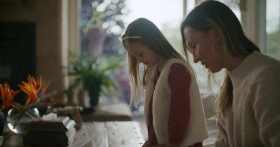 A woman plays a game with her daughter on a wooden table in the living room of a house during the day