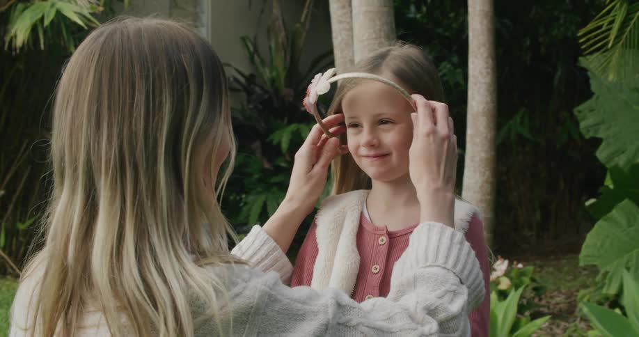 A woman smooths a little girls hair then puts in a hairband before kissing her