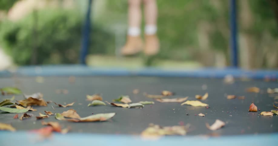 A girl jumps on a trampoline with leaves on it