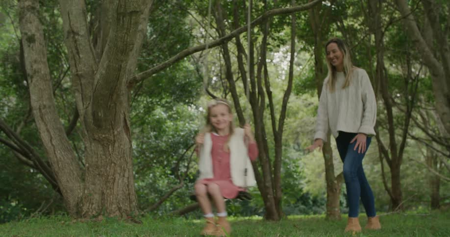 A woman pushes a young girl on a tree swing outdoors during the day