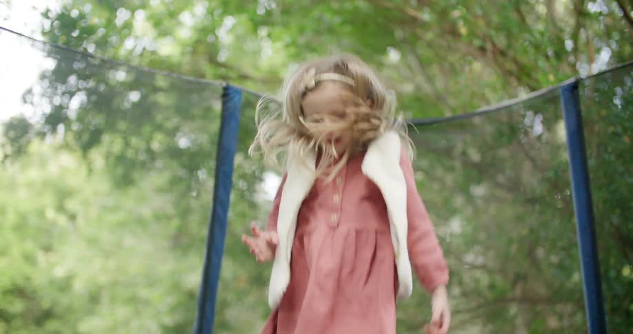 A young girl jumps on a trampoline in her backyard