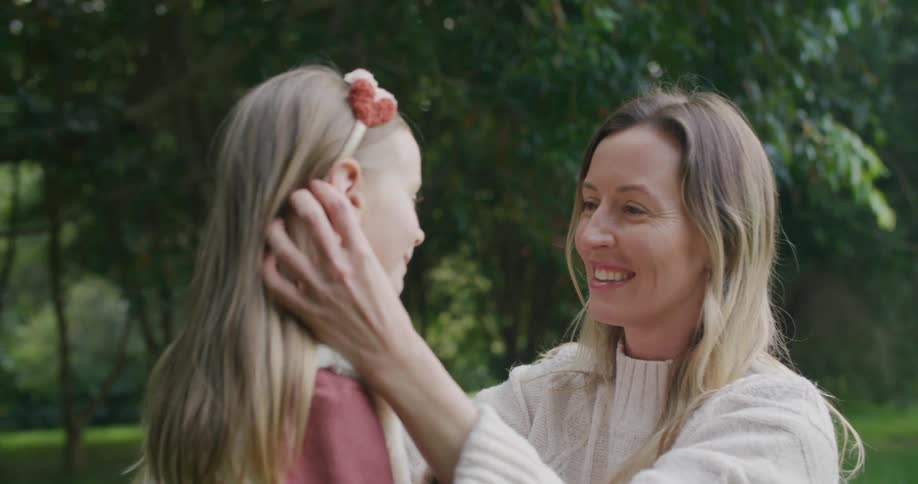 A woman putting a headband on a girls hair and kissing her with trees in the background