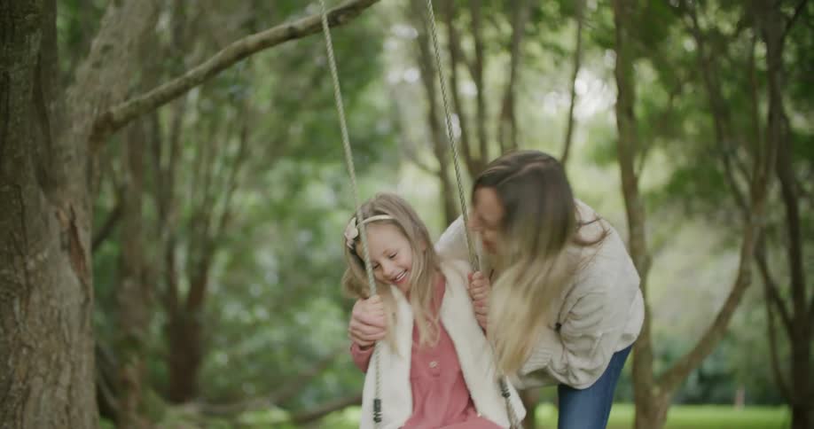 Mother and daughter playing on a swing hanging from a tree in the park