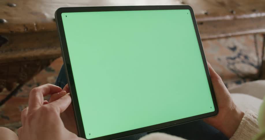 A woman sits and holds her tablet with both hands