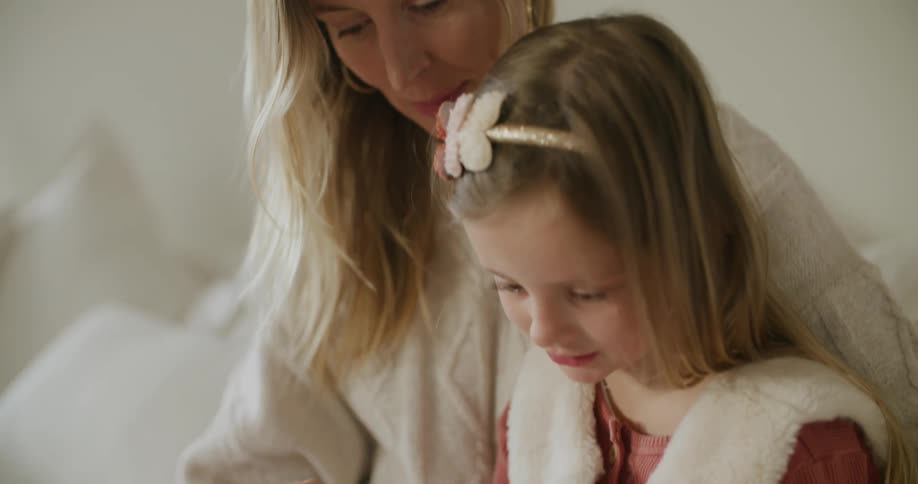 A woman sits closely with her young daughter tapping a tablet
