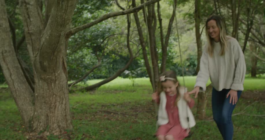 A mother pushes her daughter in the swing
