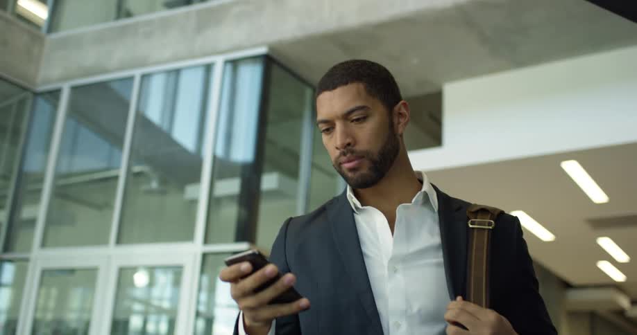 A man checks his cell phone while walking out of an office building