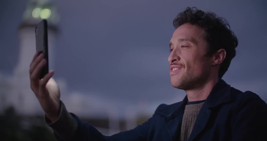 A man video chatting on his phone outside blows a kiss as he says good bye