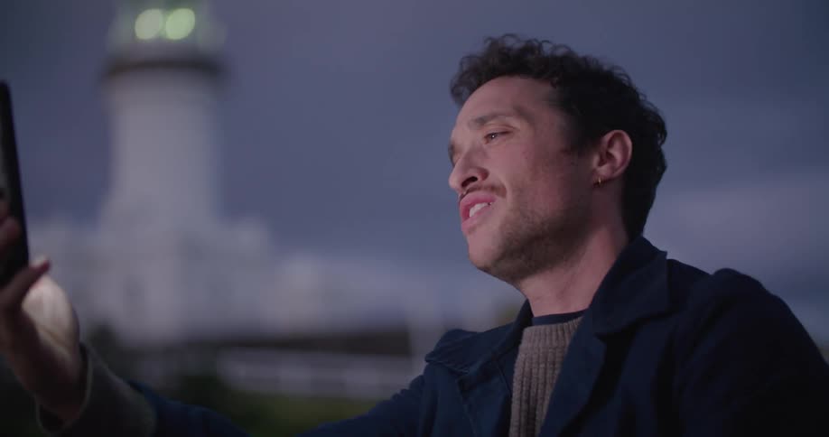 A man waves and moves his phone around so his caller can see the lighthouse behind him