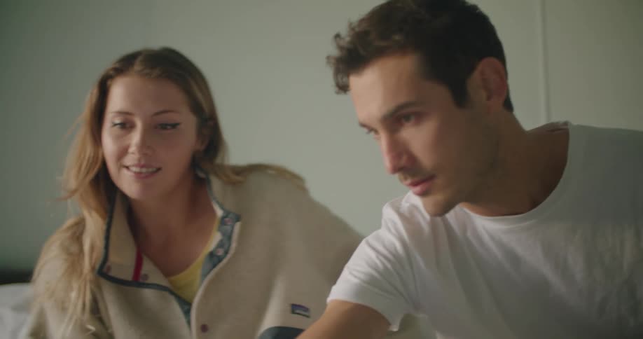 A man and woman sit in bed together while using a laptop