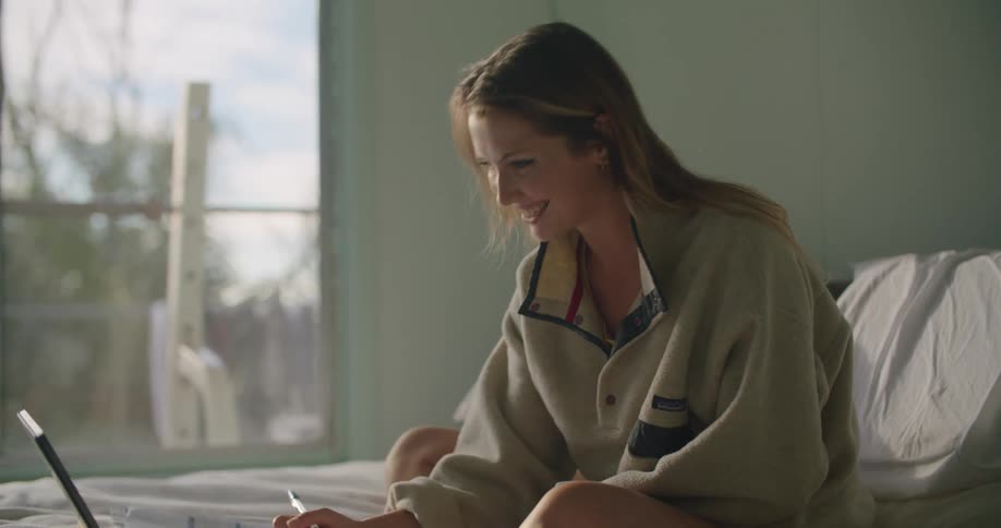 Woman sitting in the bed smiling while working on a laptop in the morning