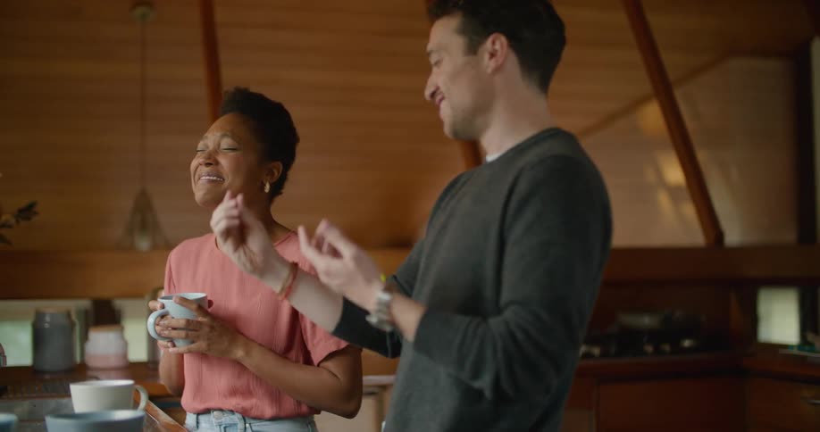 A man feeds his girlfriend food from a charcuterie board as they stand in the kitchen