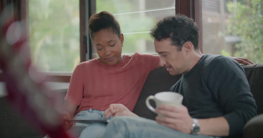 A man and a woman in a room sitting on a couch looking at a tablet