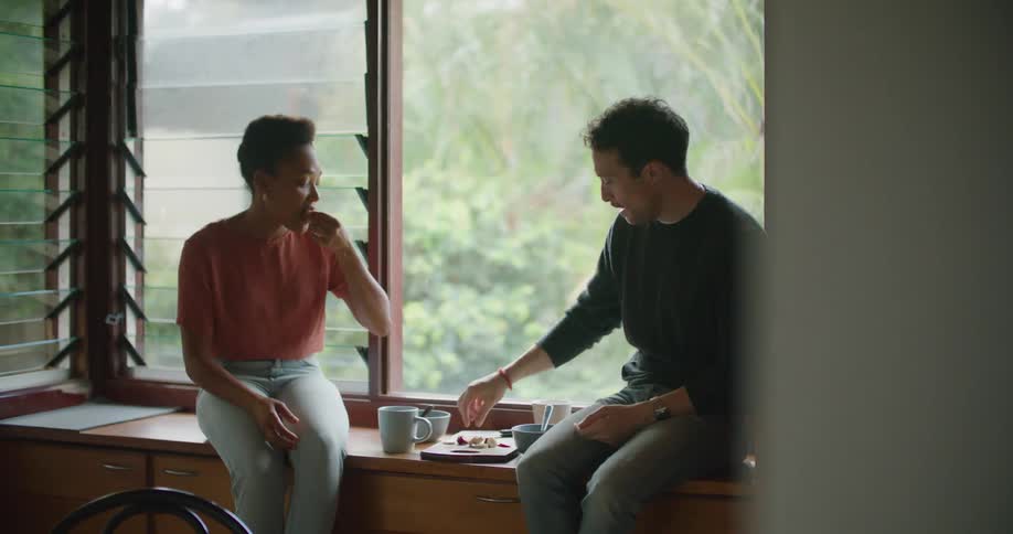 Man and woman sit near window talking and eating