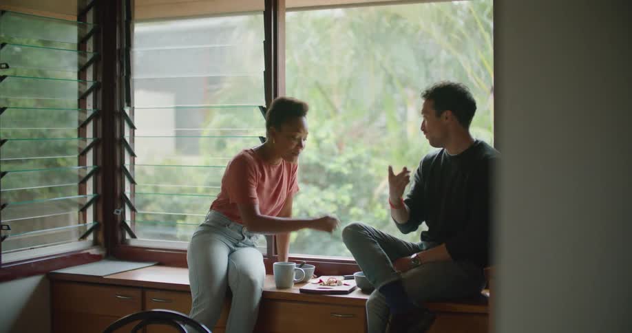 People sit near window nibbling on food on wooden board as they talk