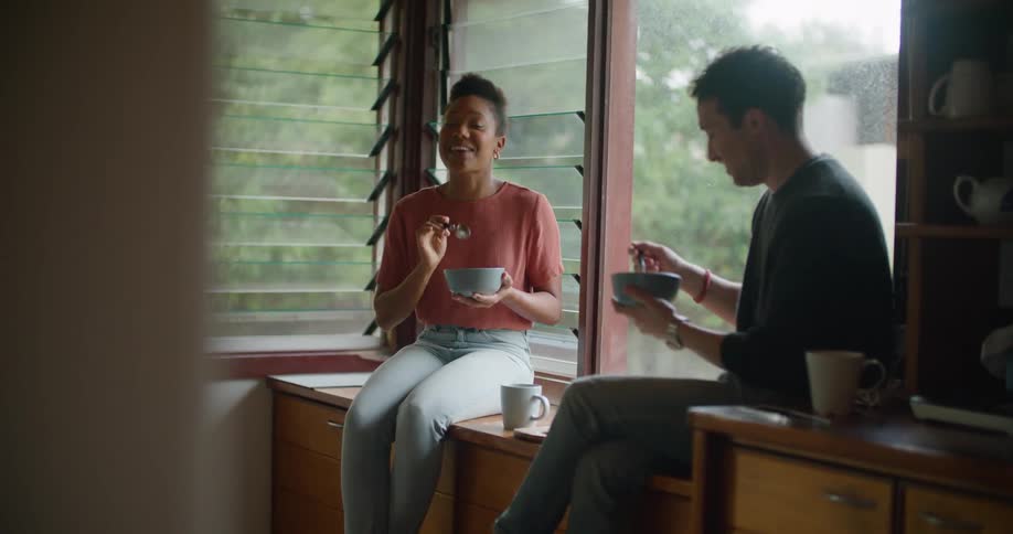 A man and woman eat and talk in the kitchen