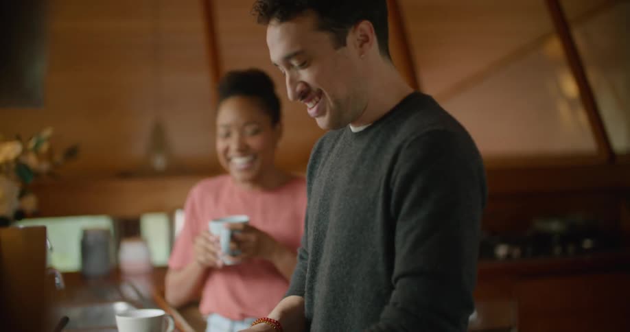 A man and a woman in the kitchen with a man cutting strawberries on a cutting board with a knife