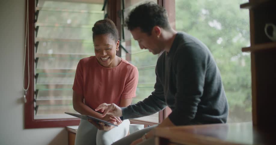 Man and woman sitting on windowpane uses tablet and laugh together