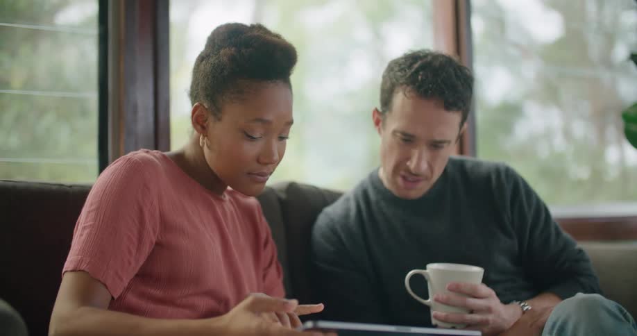 A woman sighs and looks frustrated as she discusses something on a tablet with a man sitting beside her