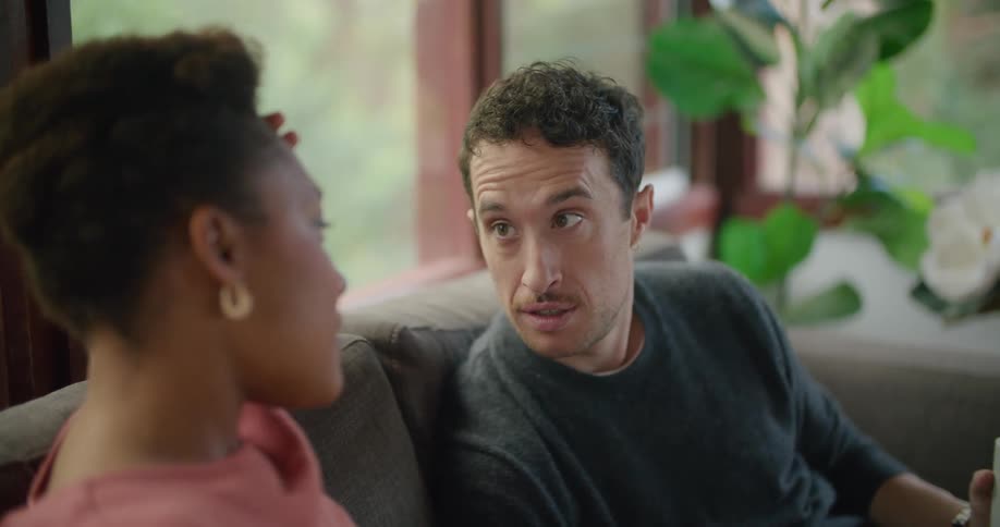 A man and woman engage in conversation while sitting together on a sofa in a house during the day