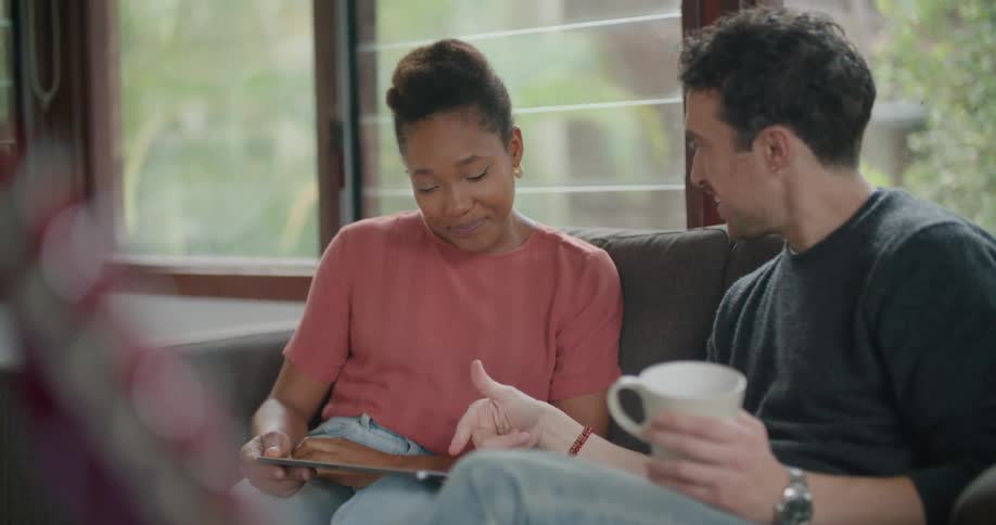 Two friends sitting in a couch talking and laughing while looking at a tablet