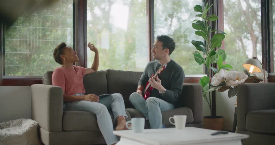 Man playing guitar to a friend sitting in the couch at home