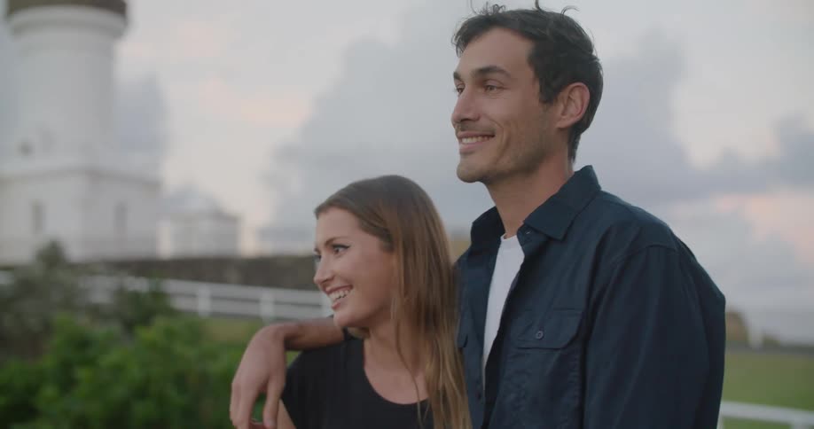 A man with his arm around a woman leans down and kisses her on the side of the face