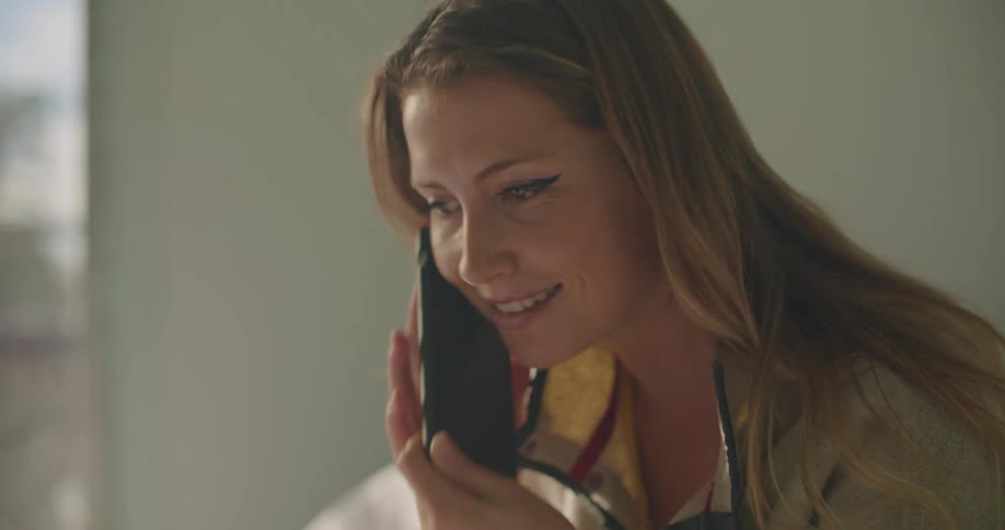 Woman sits on bed nodding while talking on phone before hanging up and writing on notepad next to tablet