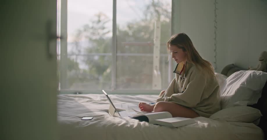 Blonde woman with oversized sweatshirt sits on bed and writes in notebook