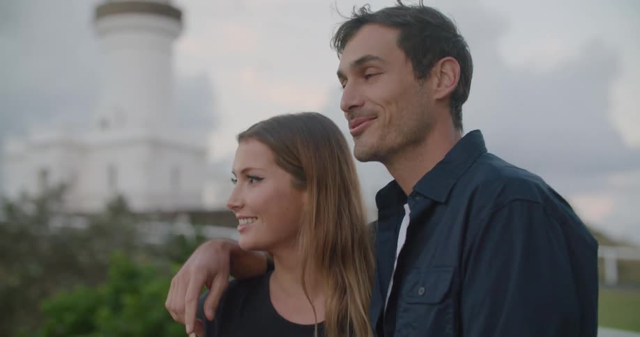 A man rests his arm around a womans shoulder as they look around at their surroundings outdoors during the day