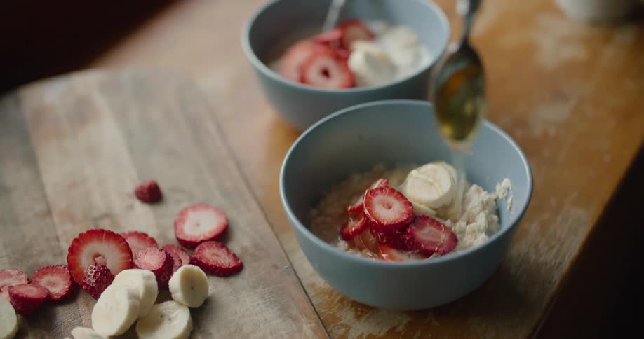 Honey dripping from a spoon into a bowl with breakfast