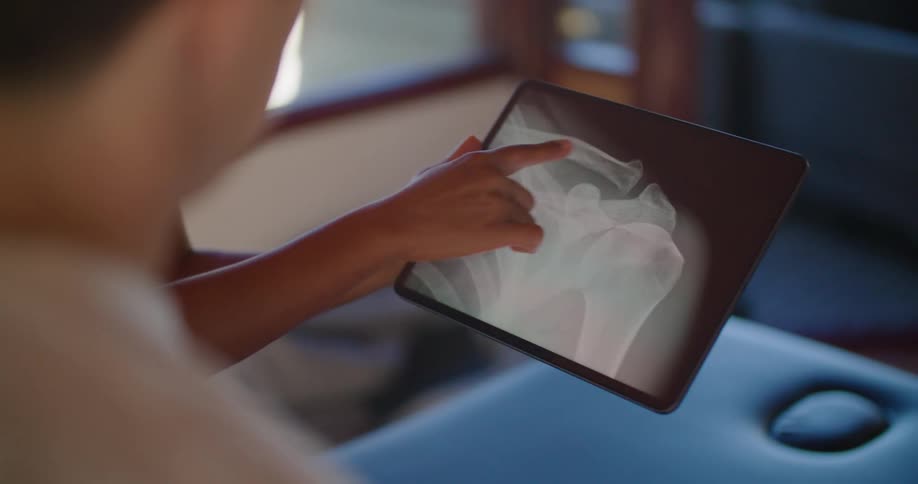 A doctor points at and zooms in on an xray displayed on a tablet as she talks with a man